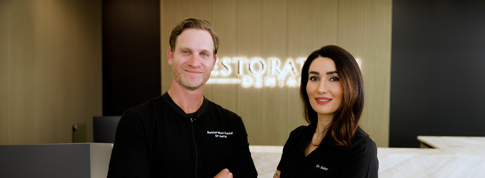 The image shows a group of people, possibly professionals given their attire and the setting that appears to be an office or professional environment. They are gathered around a table with a laptop on it, engaged in what seems to be a discussion or meeting.